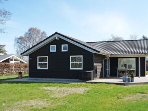Une maison noire, de plain-pied, avec un toit recouvert de tuiles, un porche à l’avant et le numéro « 67 » peint sur le côté.