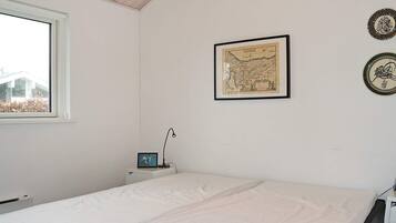 A room with a bed, a desk with a lamp, a framed map on the wall, and a window.