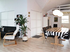 A modern living room with a sofa, a dining table with chairs, a potted plant, and a wall clock. - 10 Person Holiday Home in Hadsund-by Traum (Hadsund)