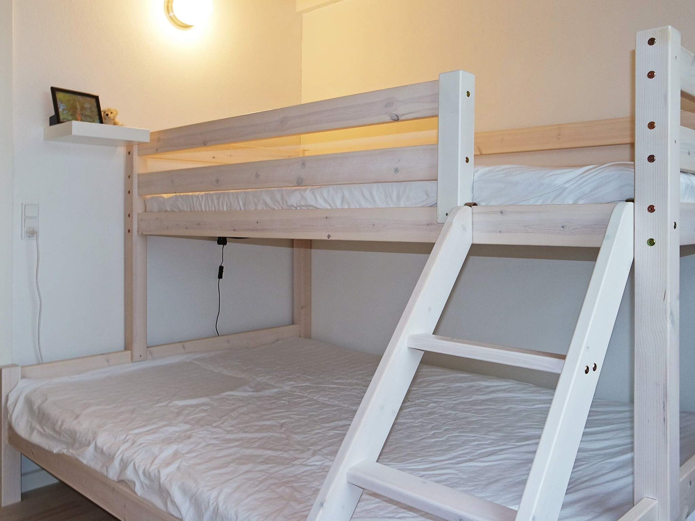 A bunk bed with a ladder, a bedside table, and a wall-mounted shelf with a picture.