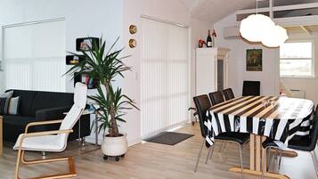 A modern living space with a dining area, a sofa, a chair, a potted plant, and a table with chairs.