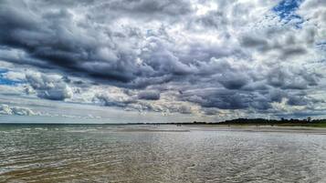 A beach with a wide expanse of sand and water, under a cloudy sky.