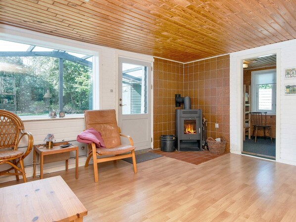 A cozy room with a wooden floor, a large window, a fireplace, and a wicker chair.