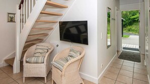 Ein modernes Interieur mit einer Holztreppe, Korbstühlen, einem Flachbildfernseher und einer zur Außenseite führenden Tür.