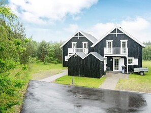 A two-story black wooden house with a balcony, a driveway, and a truck parked outside.