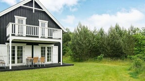 Ein zweistöckiges Haus mit Balkon, einem grünen Rasen und einem dichten Wald im Hintergrund.