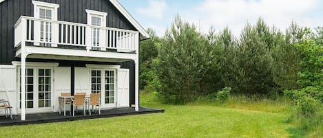 A two-story house with a balcony, a grassy yard, and a dense forest in the background.