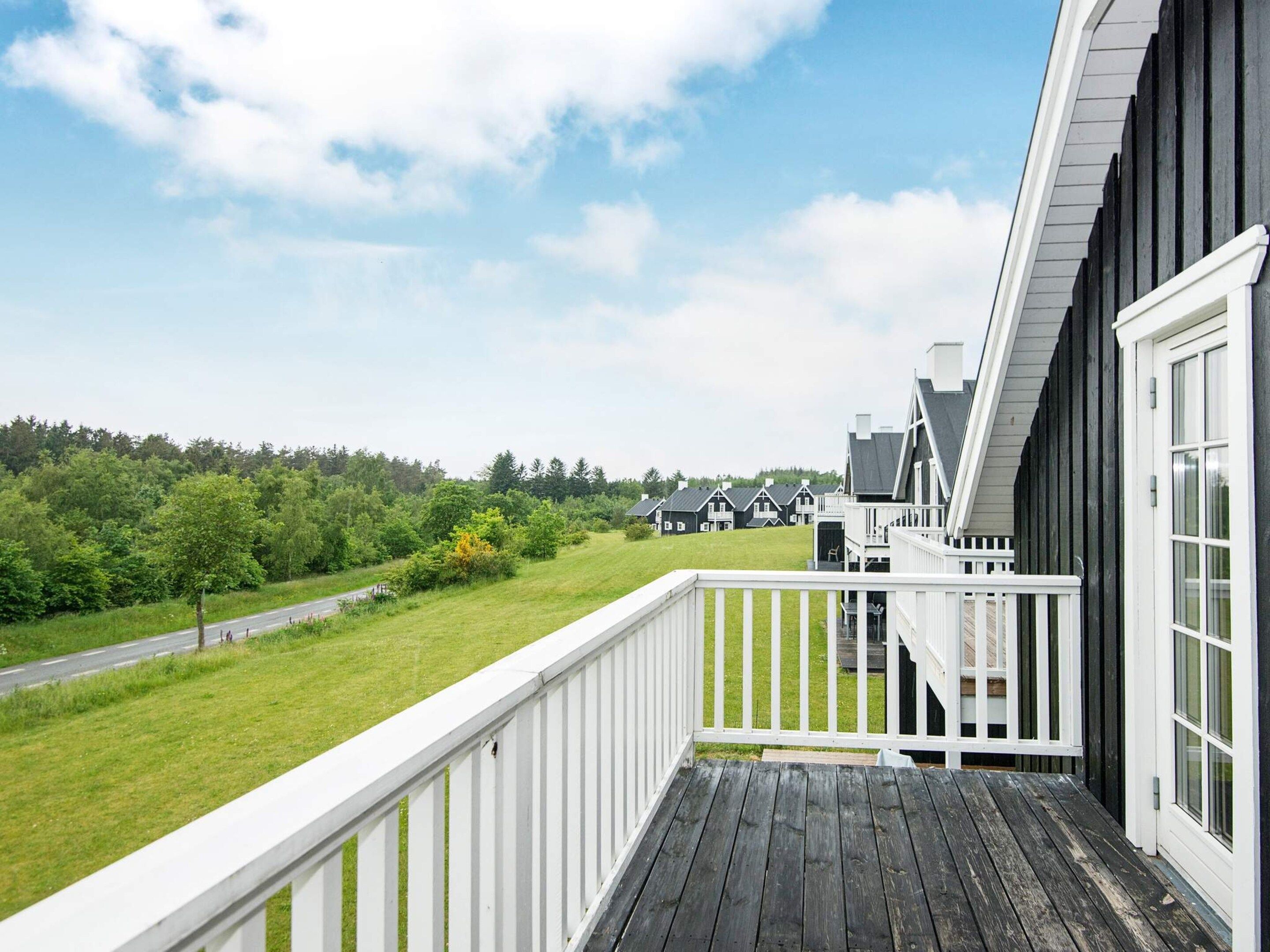 A wooden deck with a white railing overlooking a grassy area and a road.