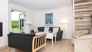 Ein Zimmer mit einer Couch, einem kleinen Tisch, einer Lampe, einem Korbstuhl und einem Bild an der Wand.