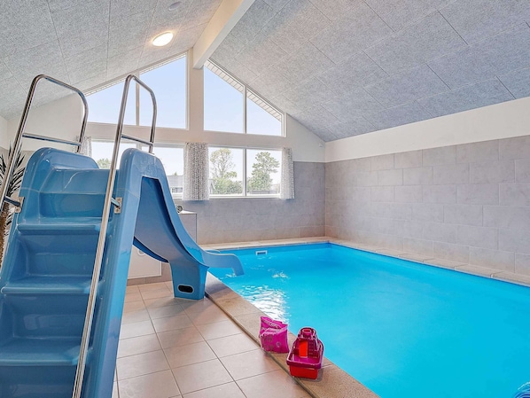 An indoor swimming pool with a blue slide, clear windows, and tiled walls. - 5 Star Holiday Home in Grenaa (Grenaa)
