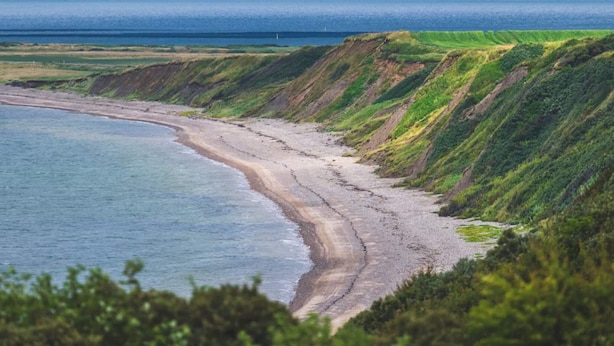 Eine Küstenlandschaft mit Strand, grasbewachsenen Klippen und weiter Meerblick.