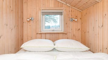 A wooden room with a bed, two bedside lamps, and a window with a view of trees.