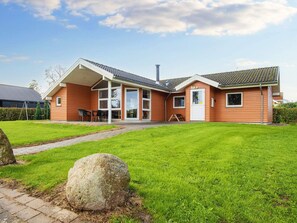 Een tweelaags huis met een overdekte patio, een groot gazon en een stenen element op de voorgrond.