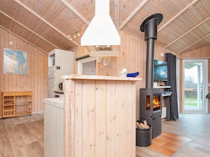 Een gezellig cabin interieur met een centraal houten eiland, een zwart houten kachel en een televisie aan de muur.
