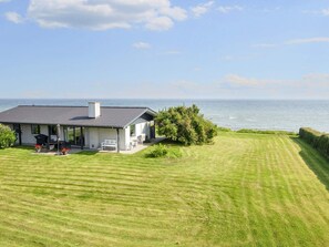 A house with a patio, a view of the sea, and a well-maintained lawn. - 6 Person Holiday Home in Odder (Odder)