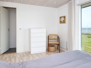 A bedroom with a bed, a chair, a wardrobe, a window with a view, and a door.