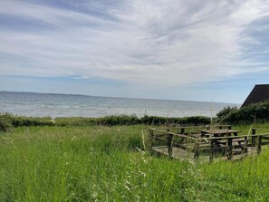 A grassy area with a wooden structure near the sea, a clear sky, and a distant view of the horizon.
