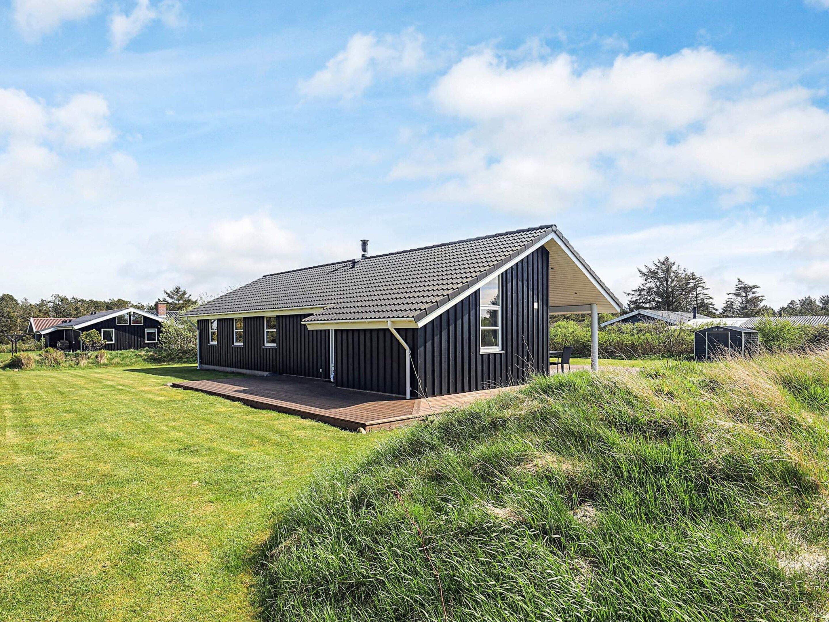 A modern house with a large deck, surrounded by a grassy area and trees.
