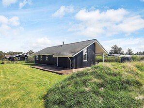 A modern house with a large deck, surrounded by a grassy area and trees.
