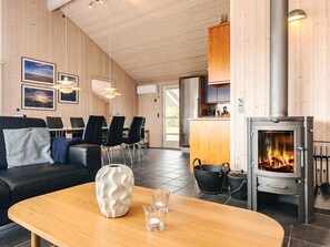 A cozy room with a fireplace, wooden walls, a dining area, and a sofa.