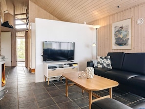 A modern living room with a flat-screen TV, a black sofa, a wooden coffee table, and a fireplace. - 5 Star Holiday Home in Lokken (Lokken)