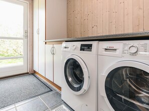 A laundry room with two front-loading washing machines, a wooden cabinet above, and a door leading outside. - 5 Star Holiday Home in Lokken (Lokken)