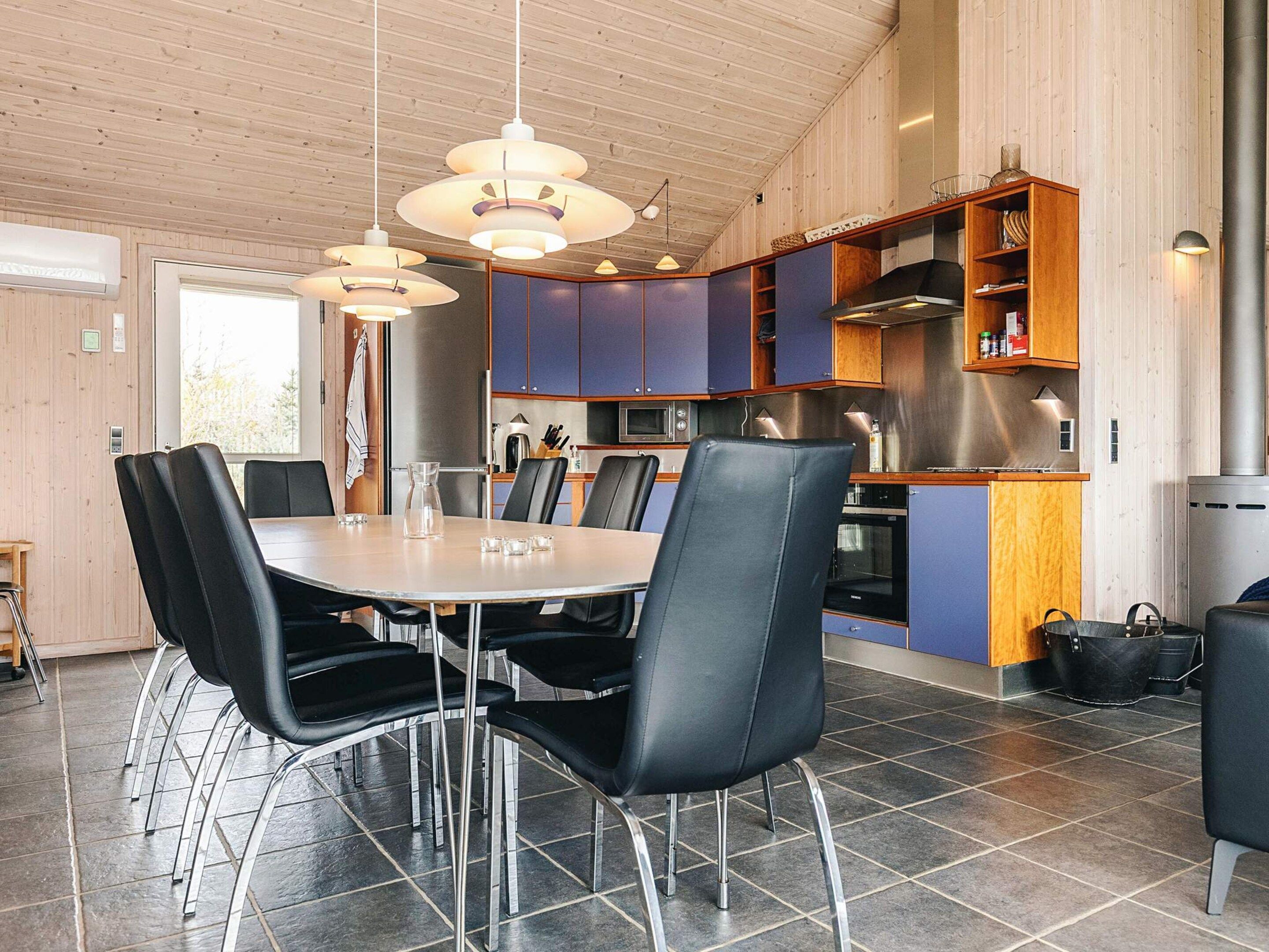 A modern kitchen with a dining area, featuring a round table with chairs, pendant lighting, and built-in cabinets.