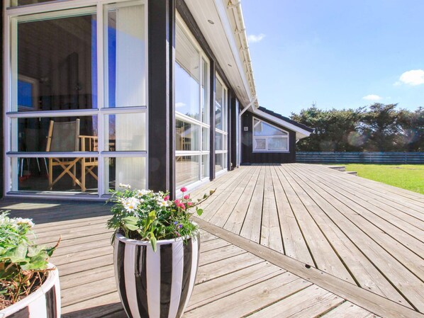 A wooden deck leading to a modern house with large windows and a potted plant.