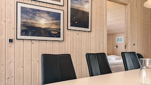 A room with a wooden paneled wall, a large table, and four black chairs. There are three small candles on the table. - 5 Star Holiday Home in Lokken (Lokken)