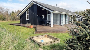 A modern black building with a large deck, a number 69 sign, and a small garden area with a sandbox. - 5 Star Holiday Home in Lokken (Lokken)