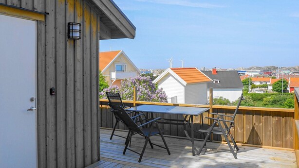 Eine Holzterrasse mit Tisch und Stühlen, mit Blick auf ein Wohngebiet mit Häusern und Windkraftanlagen.