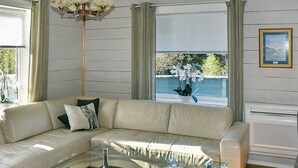 A modern living room with a beige sectional sofa, a glass coffee table, and a view of a garden through large windows. - 8 Person Holiday Home in Uggdal (Tysnes)