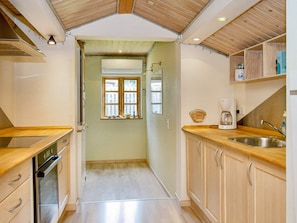A compact kitchen with wooden cabinets, a built-in oven, a coffee maker, and a window with a view.