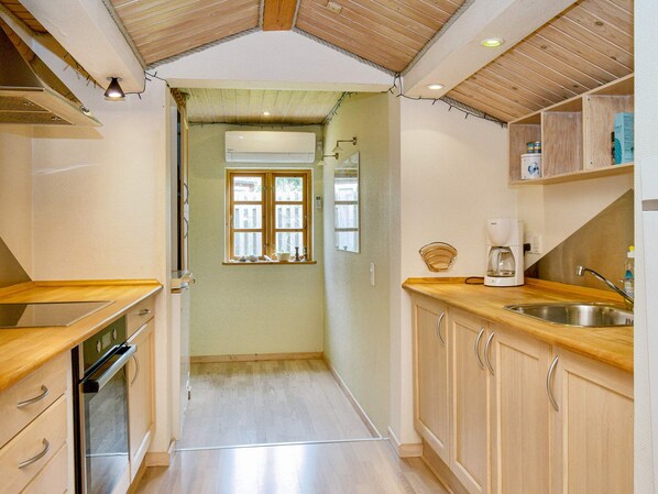 A compact kitchen with wooden cabinets, a built-in oven, a coffee maker, and a window with a view. - 9 Person Holiday Home in Jaegerspris-by Traum (Jægerspris)
