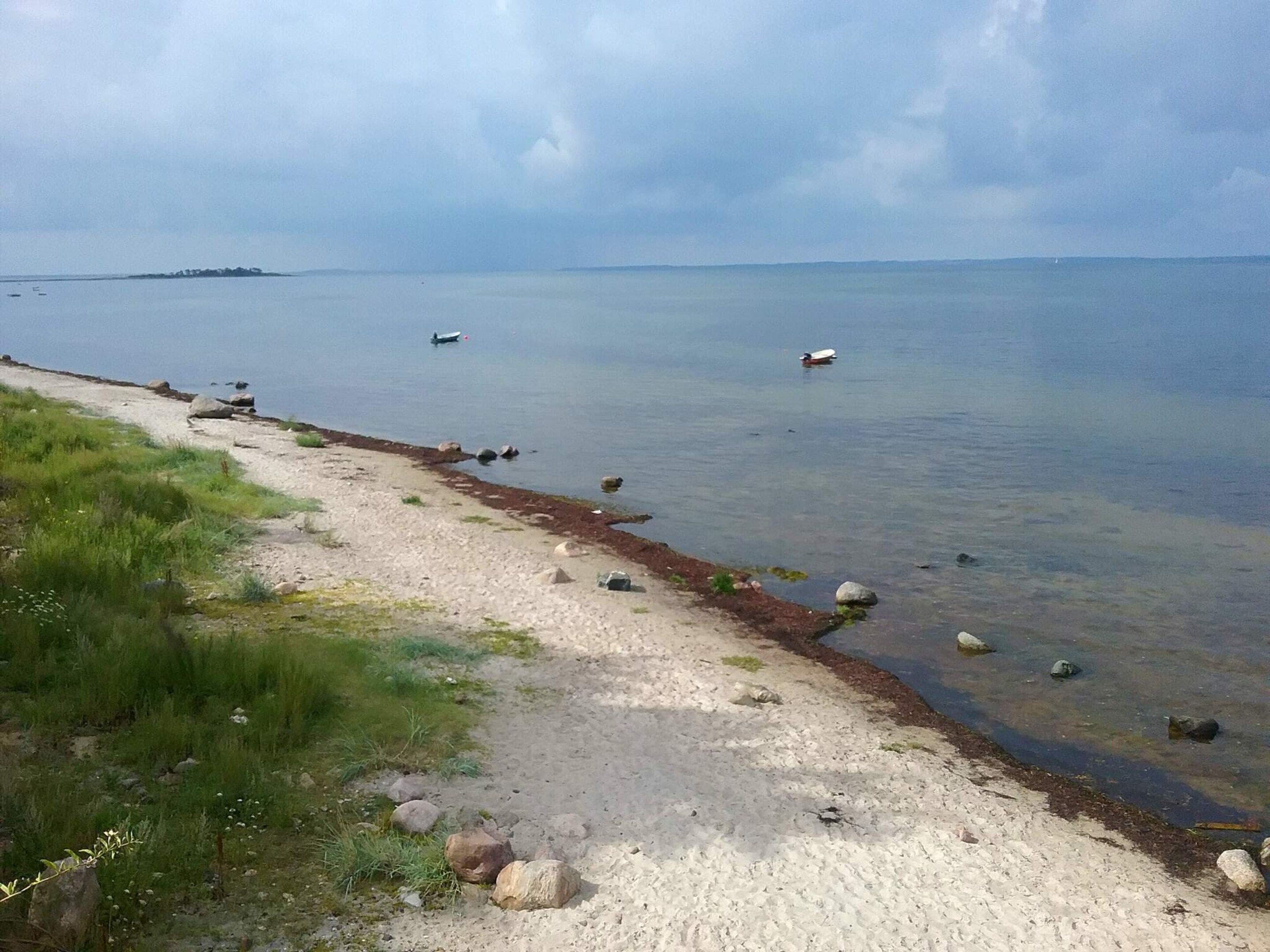 Un sendero costero con una playa de arena, rocas dispersas y un mar tranquilo.