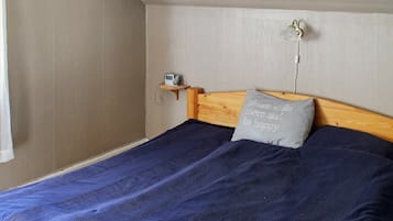 A single bed with a wooden headboard, a grey pillow with text, a bedside table with a lamp, and a wall clock.