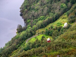 A rural landscape with a winding road, a small red house, and dense greenery. - 12 Person Holiday Home in Etne (Etne)