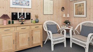 A wooden-paneled room with a wooden cabinet, two white wicker chairs, a small table with a vase, and framed artwork on the walls. - Secluded Beach Retreat - By Traum Ferienwohnungen (Skagen)