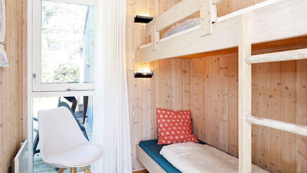 A wooden cabin room with bunk beds, a white chair, and a window with curtains. - Secluded Beach Retreat - By Traum Ferienwohnungen (Skagen)