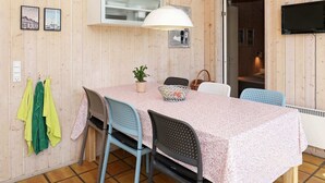 A wooden-paneled room with a dining table, chairs, a hanging lamp, and a television mounted on the wall. - Secluded Beach Retreat - By Traum Ferienwohnungen (Skagen)