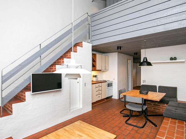 A compact kitchen with white cabinets, a dining table with chairs, a staircase, and a small seating area.