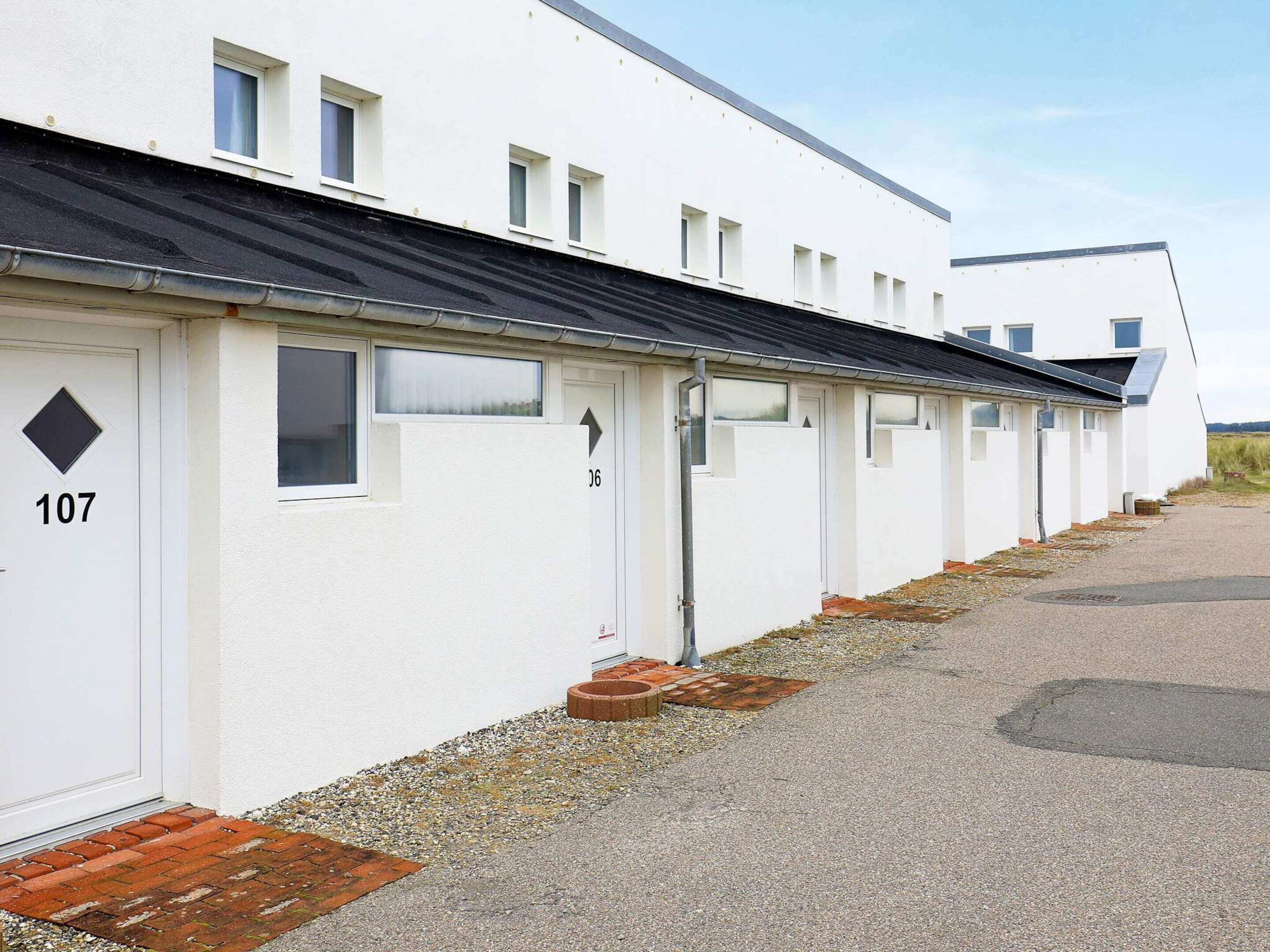 A row of white mobile homes with numbered doors, a gravel path, and a clear sky.