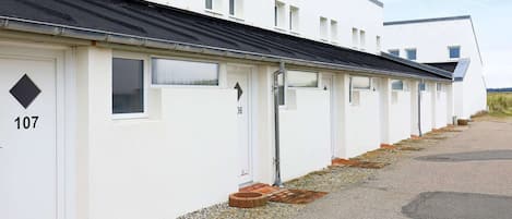 Une rangée de maisons mobiles blanches, chacune avec une porte numérotée, un chemin de gravier et un ciel dégagé.