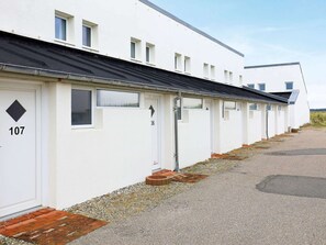 A row of white mobile homes with numbered doors, a gravel path, and a clear sky.