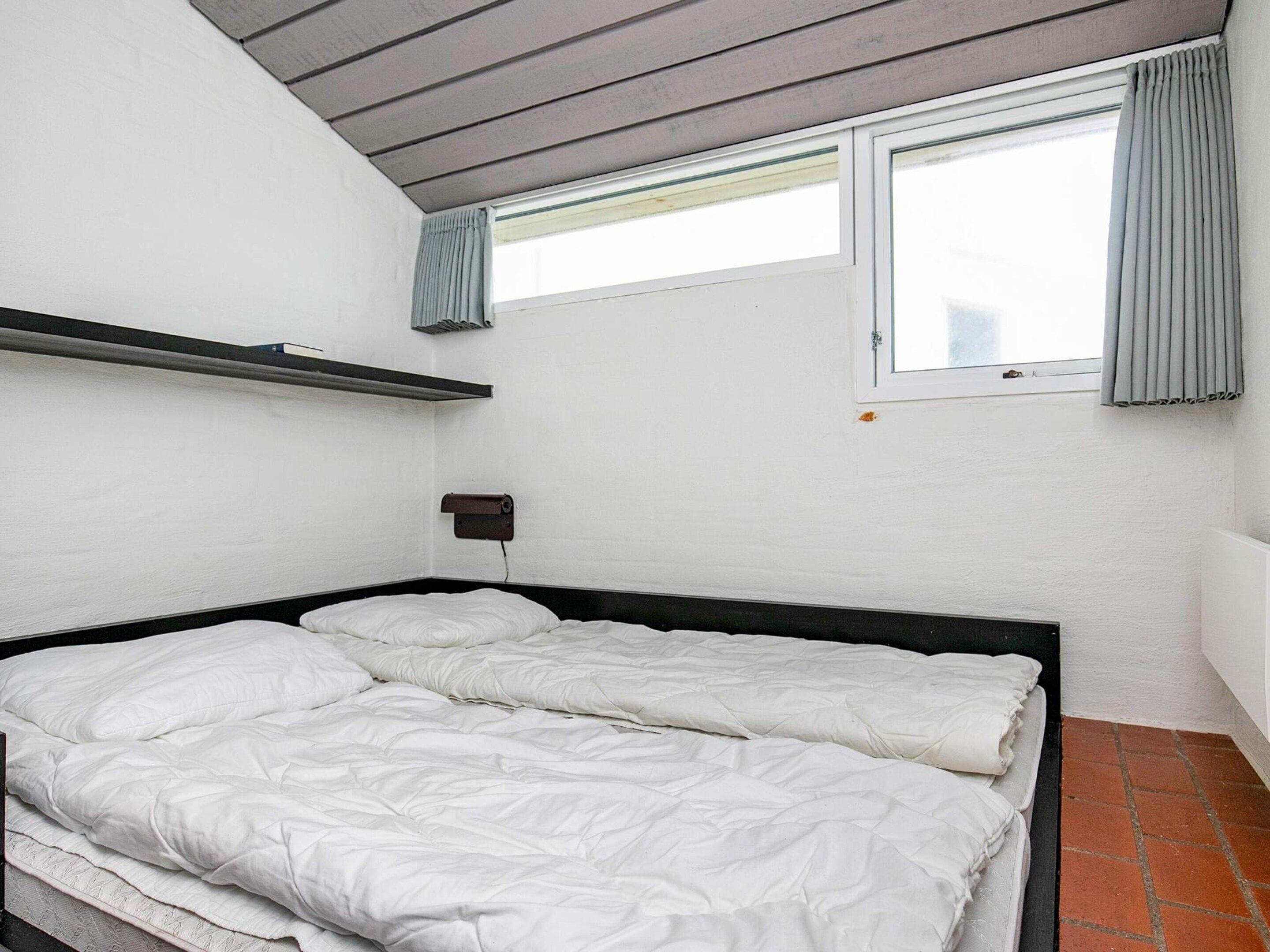Ein Einzelzimmer mit Bettkopfteil, einem Vorhangfenster, einem Wandregal und einer Heizung.