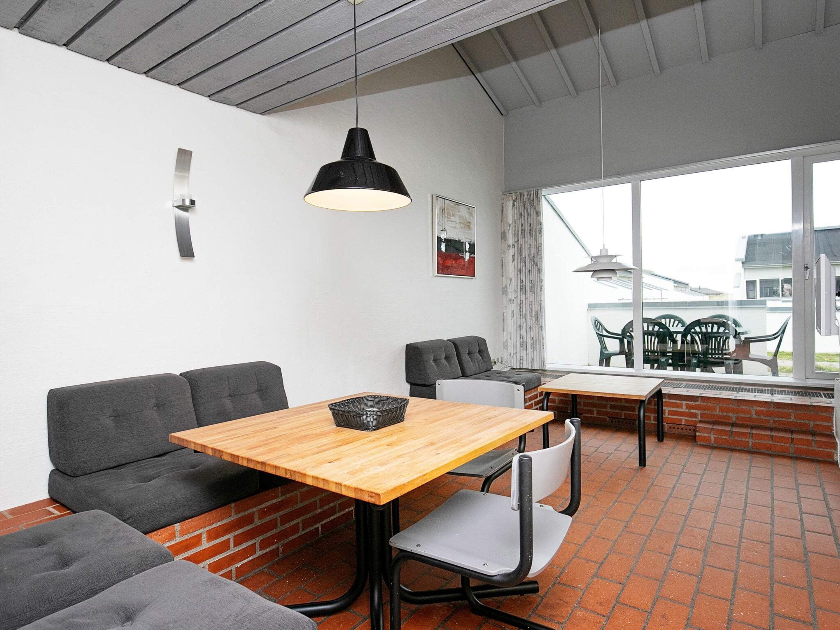 Ein modernes Interieur mit einem Holztisch, grau gepolsterten Sitzmöbeln und einem großen Fenster mit Aussicht.