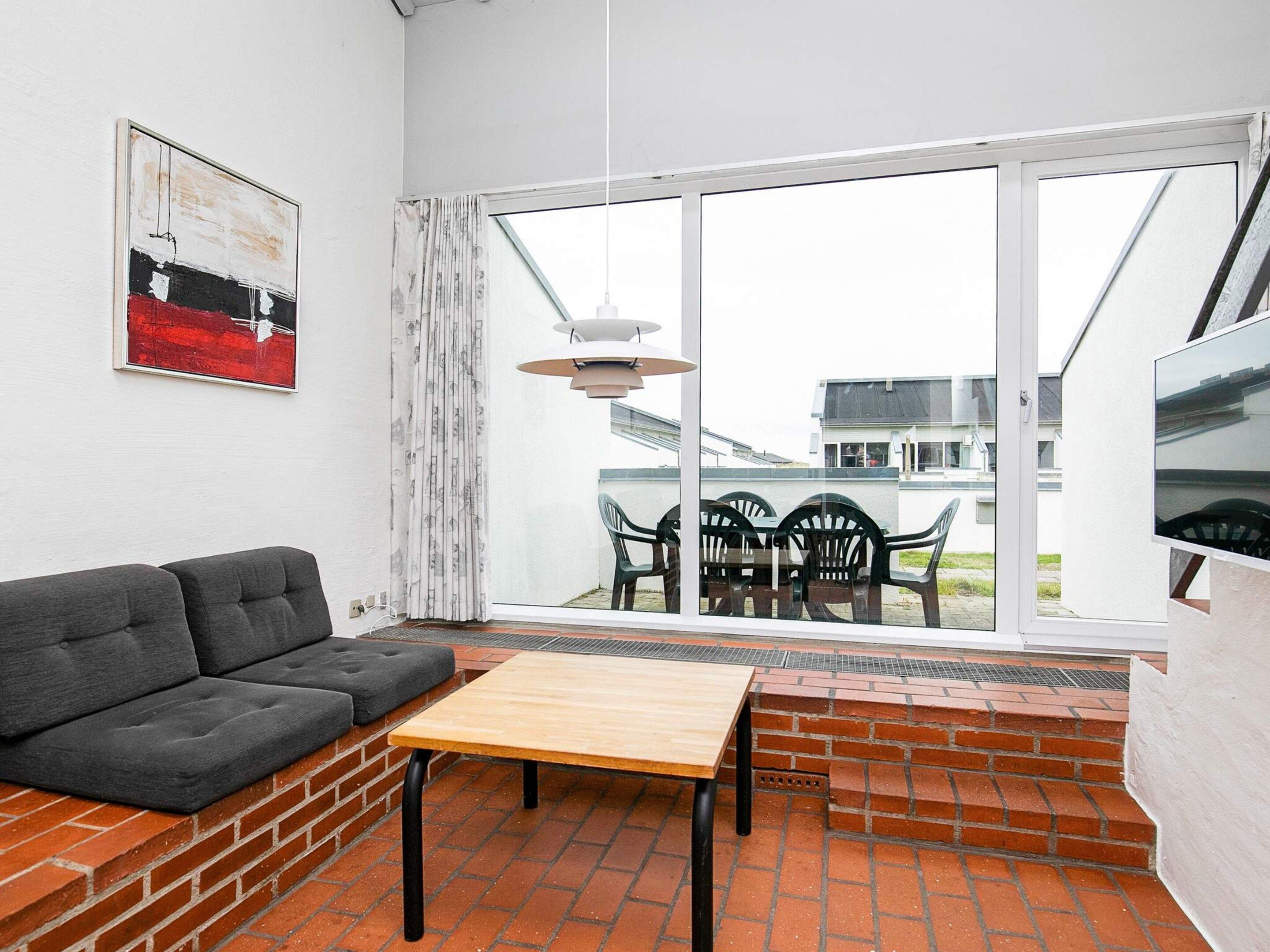 A modern living room with a sofa, a table, and a view of the outside through large windows.