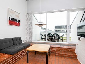 A modern living room with a sofa, a table, and a view of the outside through large windows.