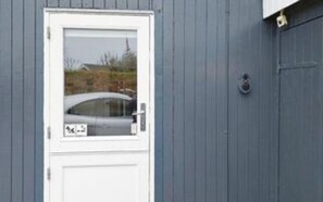 Valkoinen ovi, jossa on ikkuna, pieni postilaatikko ja metallinen ovikello.