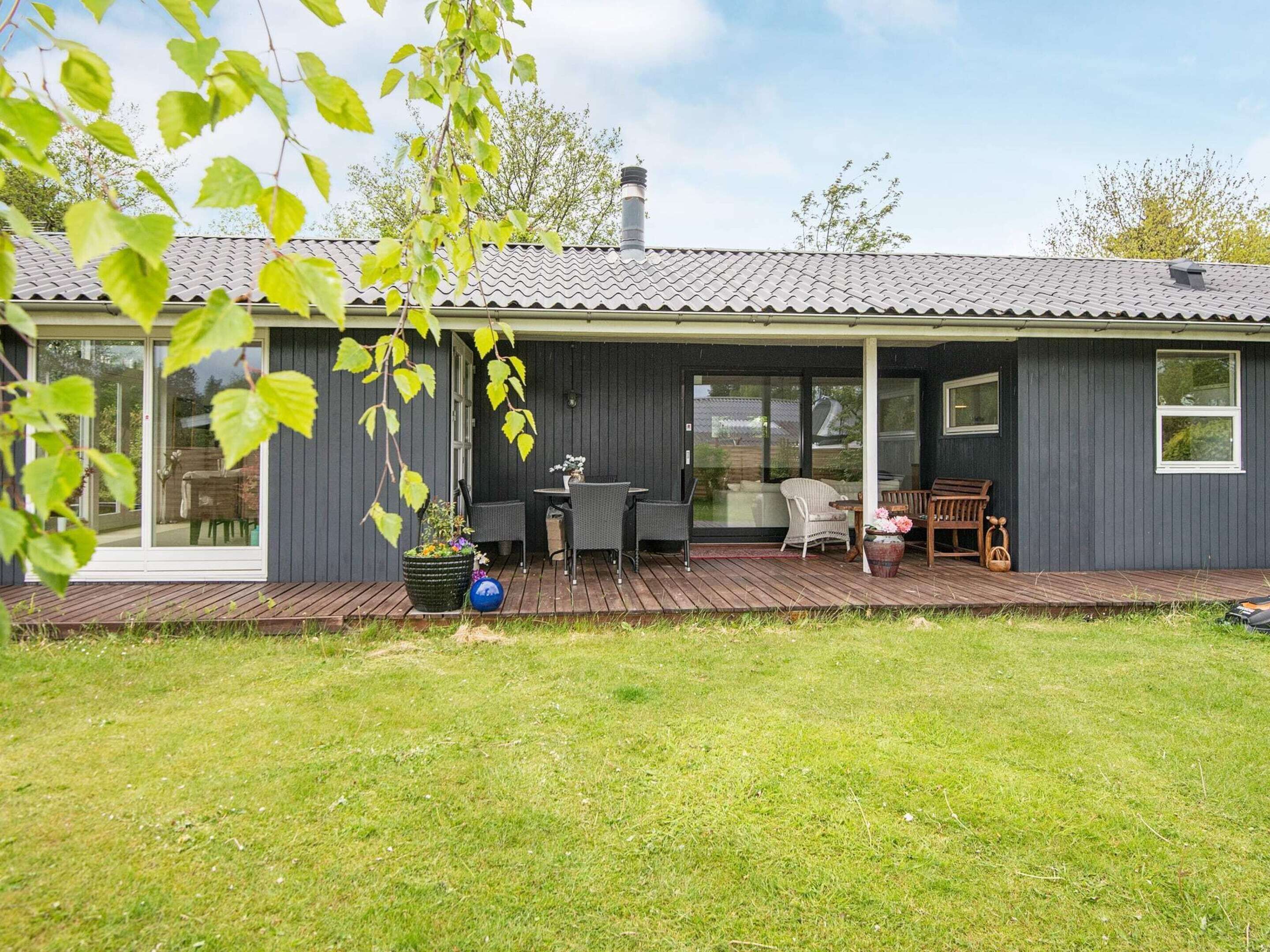 Ett modernt hus med en inglasad veranda, en matplats och en trädgård.